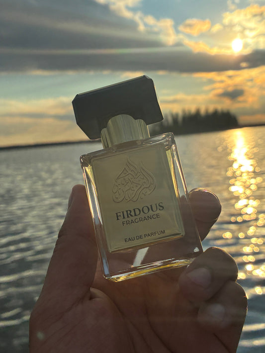 Hand holding a perfume bottle with a sunset and water background
