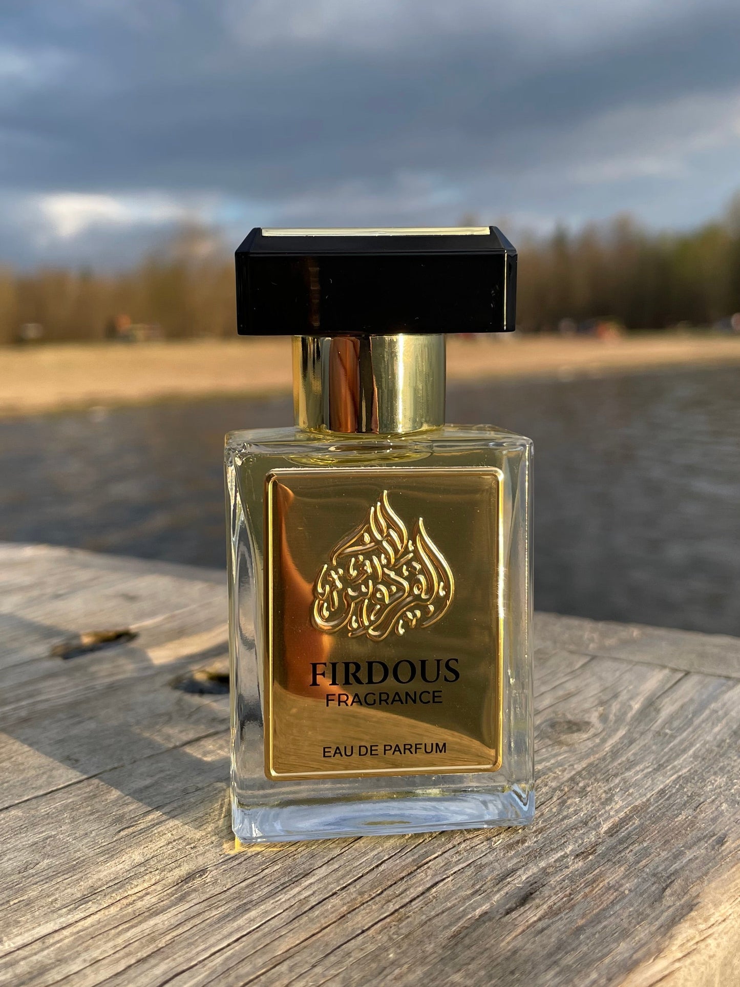 Perfume bottle with gold label on a wooden surface against a cloudy sky