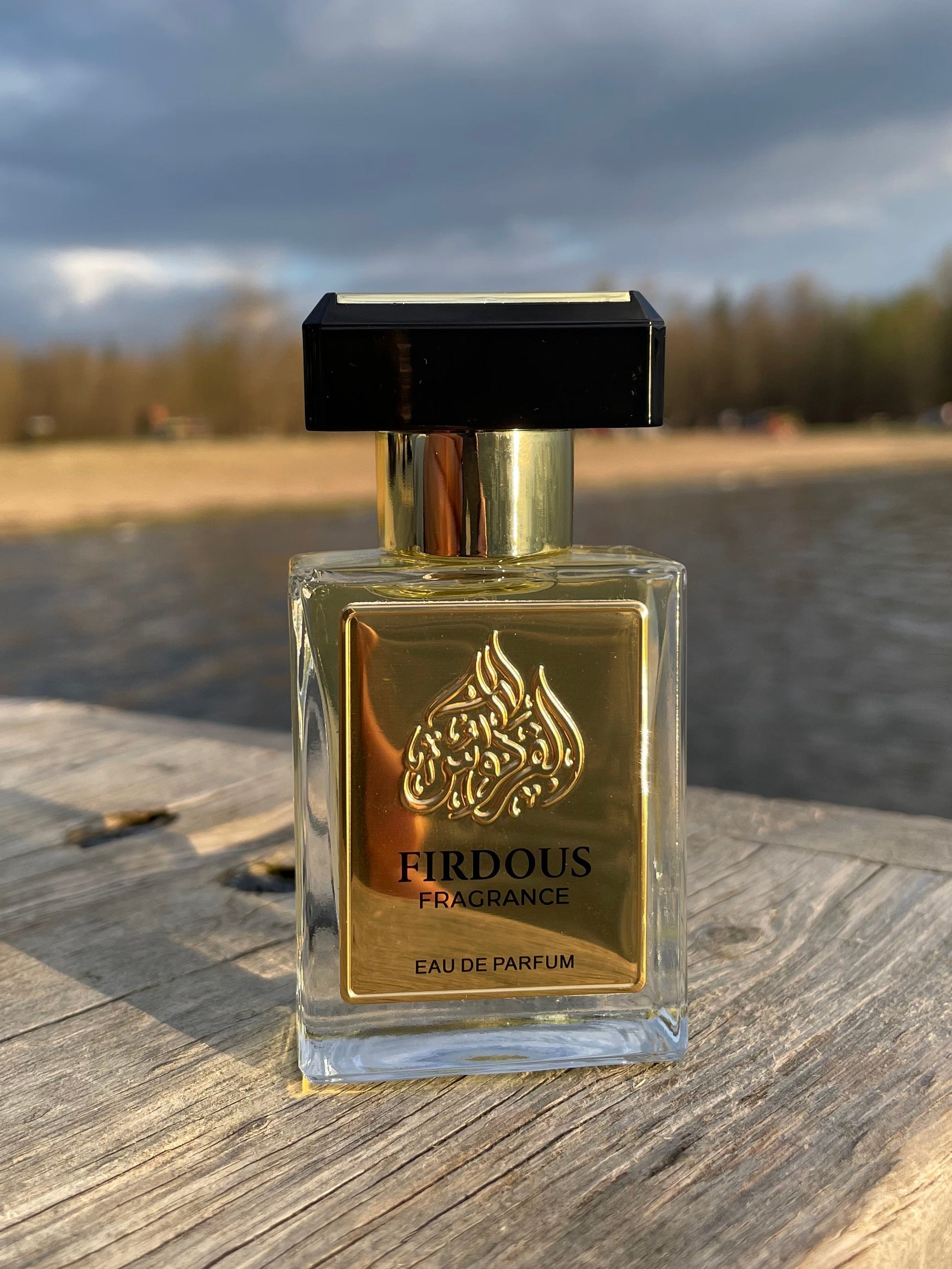 Perfume bottle with gold label on a wooden surface against a cloudy sky